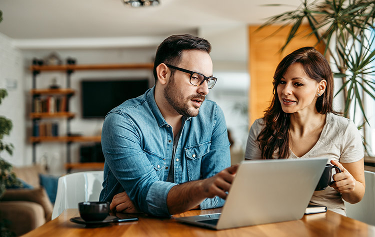 Mann und Frau sitzen im Home Office vor einem Laptop am Tisch und reden