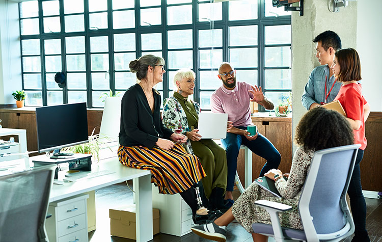 Diverse Mitarbeitende sitzen im Büro locker zusammen und unterhalten sich