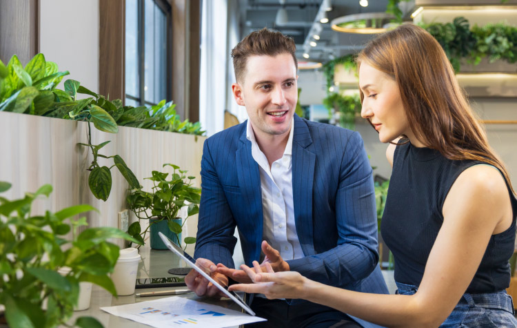 Zwei junge Mitarbeitende diskutieren miteinander in einem grünen Büro