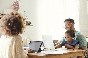 Vater, Mutter und Kind sitzen gemeinsam arbeitend am Essenstisch