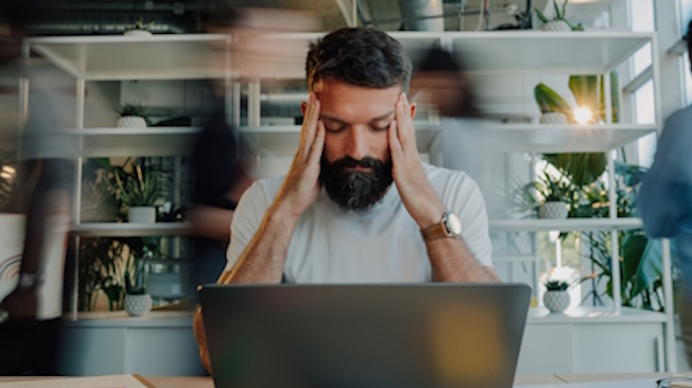 Mann sitzt vor Laptop und hält sich die Hände an den Kopf
