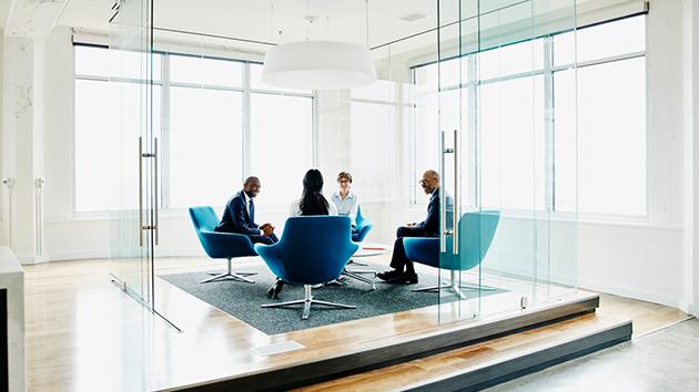 Vier Mitarbeitende haben ein Meeting in einem gläsernen Konferenz-Büro