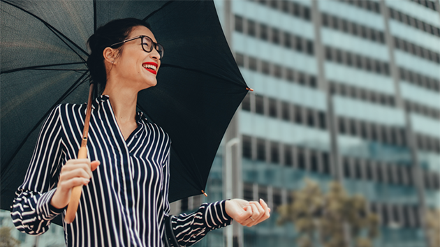 Frau mit Regenschirm steht in der Sonne uns lacht