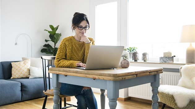 Eine Frau sitzt mit ihrem Laptop am Tisch und schreibt einen kompetenzbasierten Lebenslauf als Quereinsteigende