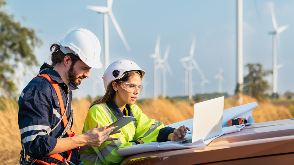 Ingenieure stehen im Feld vor Windrädern und arbeiten an Bauplänen