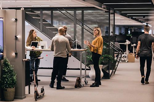 Junge Mitarbeitende stehen im modernen Büro und unterhalten sich